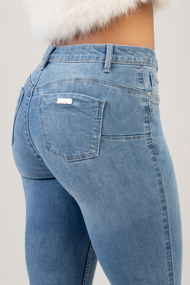 back view of light blue skinny jeans on a model, visible rear pocket with small metal brand tag and contrast stitching