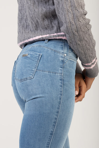 side view of light wash blue jeans on a person, back pocket with stitching and a small metal tag, paired with a grey
