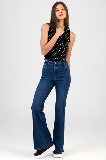 woman wearing blue flare leg jeans and a black sleeveless polka dot top with scalloped edges