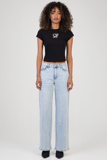 woman wearing light wash wide leg jeans with sparkly vertical stripes and a black short sleeve crop top against a plain