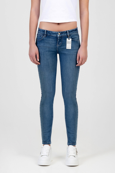 woman in blue skinny jeans with a white cropped top and white sneakers, tag hanging from the front pocket