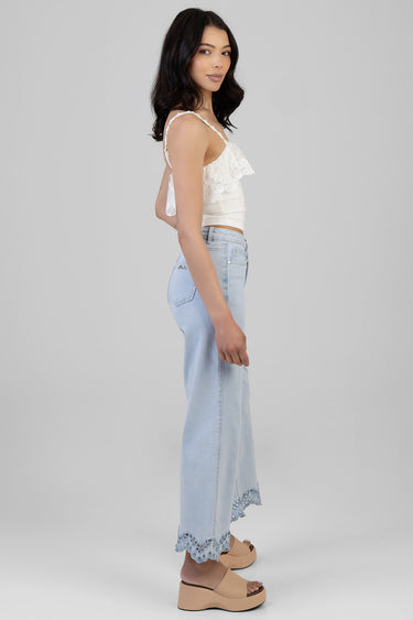 woman in white lace cropped top with shoulder straps and light blue wide leg jeans with scalloped hem