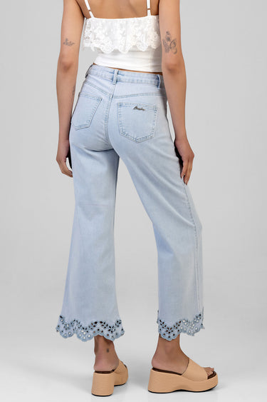 back view of a woman wearing light blue cropped wide leg jeans with scalloped lace trim at the hem and a white lace crop