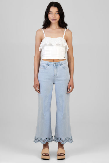 model wearing a white lace cropped top with straps and light wash wide leg jeans with scalloped lace hem