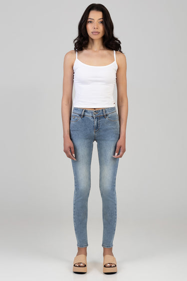 woman wearing a white tank top and light wash skinny jeans with beige platform sandals standing against a neutral backdrop