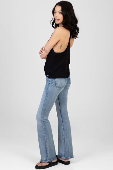 woman in a black sleeveless top and light blue bootcut jeans, standing sideways with sandals