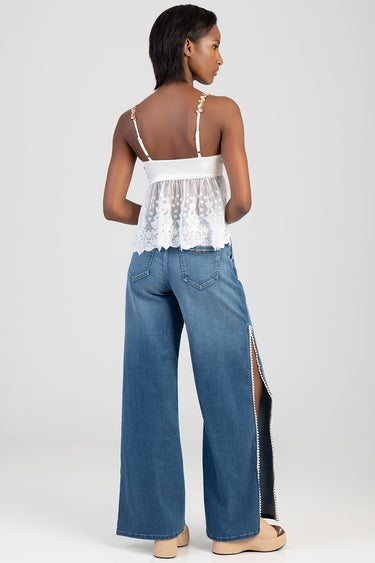 woman wearing white lace back top with floral straps and blue wide leg jeans with a side slit and pearl trim