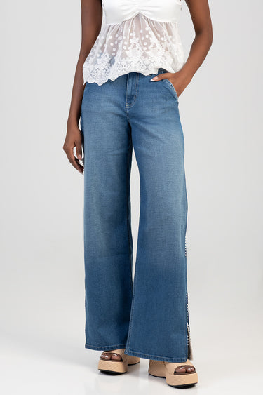woman in white lace top and blue wide leg jeans standing with one hand in a pocket