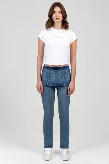 woman wearing white cropped t shirt and blue stovepipe jeans from Blue Jean Traders standing against a light backdrop