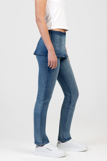 side view of a person wearing blue denim stovepipe jeans with a peplum overlay and white sneakers