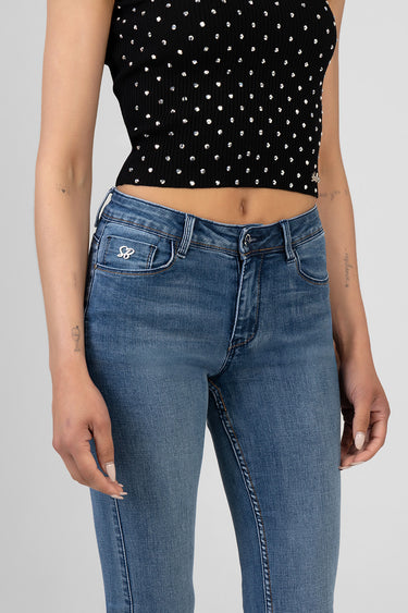 woman wearing blue skinny jeans with a faded wash and a small white logo on the coin pocket, paired with a black cropped