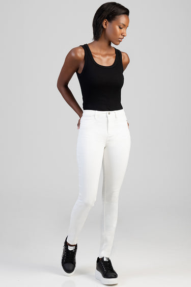 woman in white skinny jeans and black tank top standing with hands in pockets