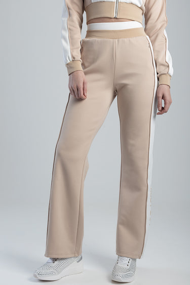 beige track pants with a white side stripe and zip pocket, paired with white studded sneakers