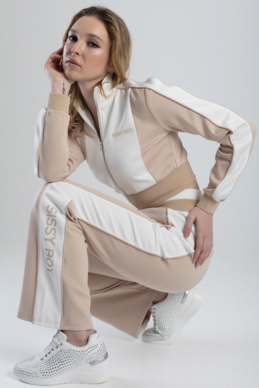 woman wearing a beige and white tracksuit with sissy boy branding, crouching in white studded sneakers