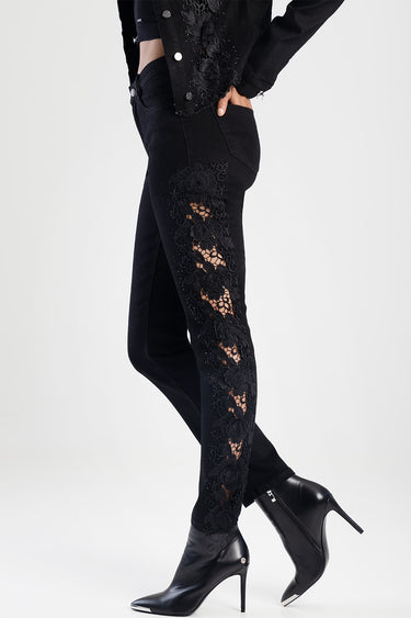woman wearing black straight jeans with floral lace panels along the outer leg, paired with black heeled ankle boots — blue