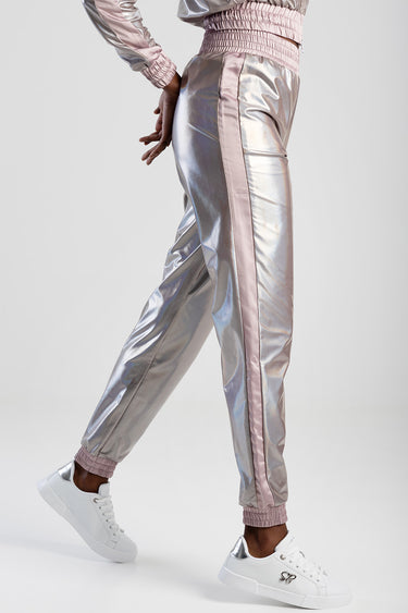 model wearing metallic pink and silver track pants with a side stripe, elastic waistband and cuffs, paired with white