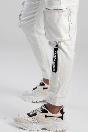 white cargo pants with a large zip pocket at the thigh, elastic cuffs, and a hanging black tag, worn with chunky sneakers