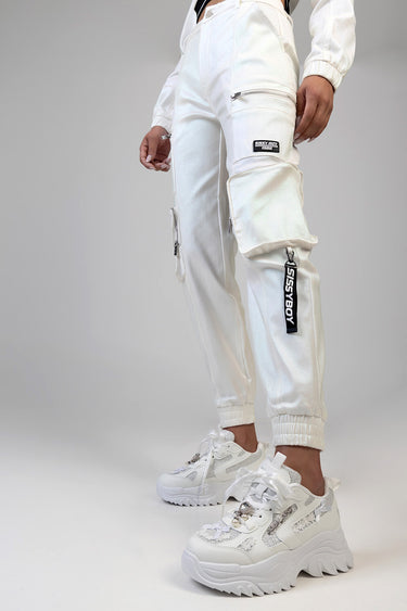 blue jean traders white cargo track pants with zip pockets and a black patch on the thigh, paired with white chunky sneakers