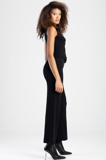 side view of a model in black ribbed knit pants and a matching sleeveless top, paired with black heeled ankle boots with