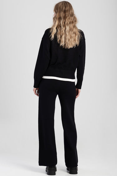 back view of a person with wavy blond hair in a black knit sweater and black wide leg pants with a white band at the hem