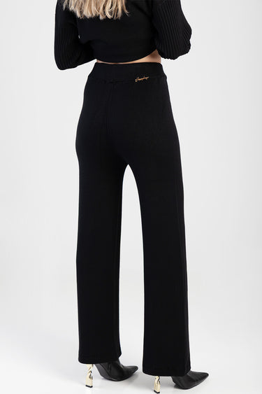 back view of black knit pants with wide legs and a small gold logo at the back waistband