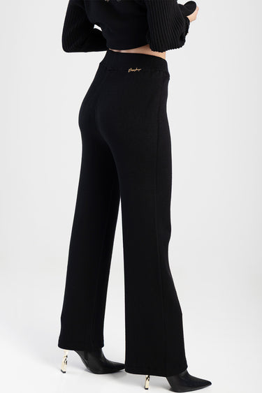 side view of black knit pants with a high back waist and wide legs, gold script logo at the back, with a black top and