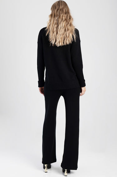 person wearing black knit pants and matching black sweater, viewed from the back