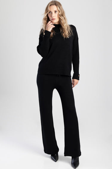 woman in a black knit sweater and wide leg knit pants with heeled boots against a light backdrop