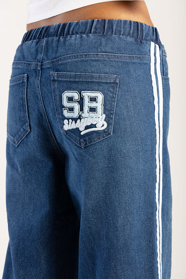blue denim jeans with white side stripes and a back pocket embroidered with light blue initials sb and cursive script