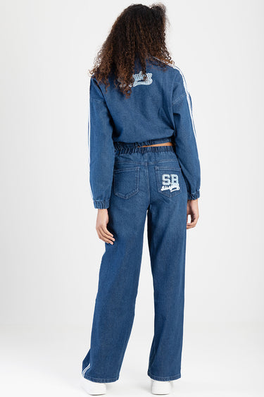 back view of person wearing blue denim track jeans with patch on the right back pocket and elastic waistband; matching