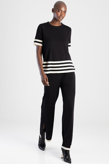 woman in black knit pants with white striped cuffs and hem, wearing a black short sleeve top with matching stripes