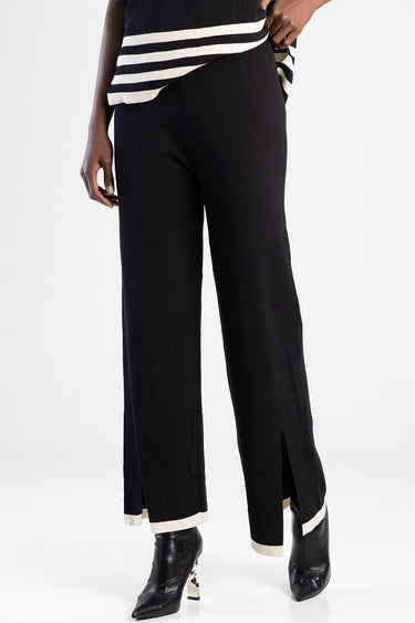 woman wearing black knit wide leg pants with cream cuffs and front slits, paired with a striped top and black ankle boots
