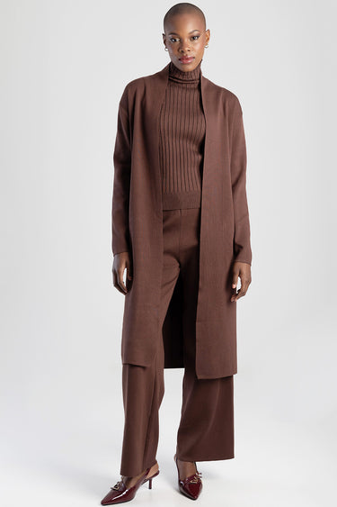 model wearing a brown knit turtleneck with matching brown knit wide leg pants and a long coat with burgundy heels