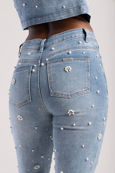 back view of light blue denim jeans with pearl bead embellishments and a small silver badge on the back pocket