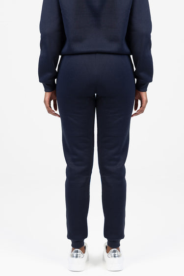 back view of a person in navy blue track pants with cuffed ankles and a matching top, white sneakers with silver heel accents