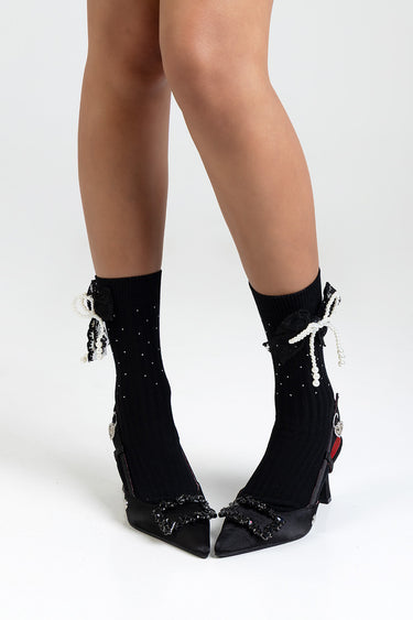 legs in black socks with pearl bow embellishments and black pointed heels