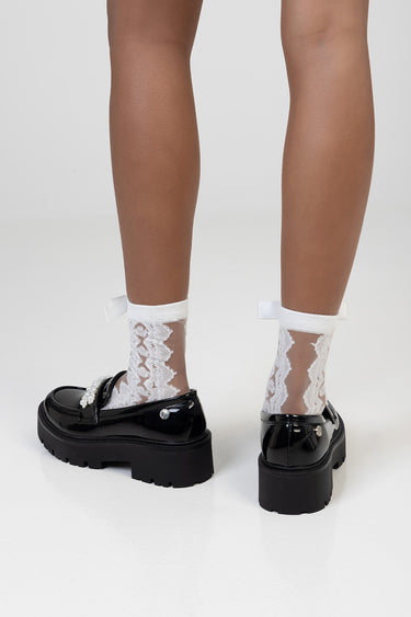 legs wearing white lace socks with bows and pearl embellishments on black chunky platform loafers