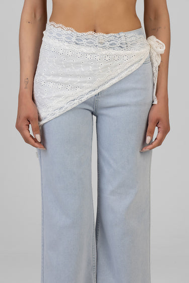 white lace wrap tied at the waist over light wash denim jeans with a floral eyelet pattern and scalloped edges
