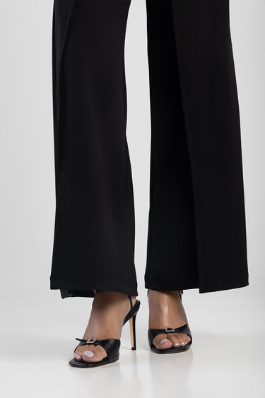 woman wearing black heeled sandals with a thin strap and buckle, paired with wide leg black pants