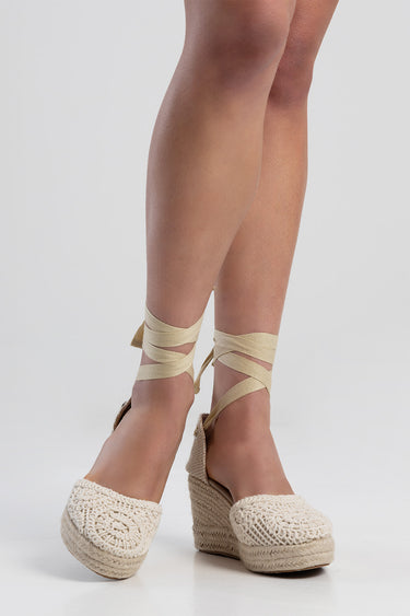 woman wearing beige crochet wedge espadrilles with cream ankle wrap straps against a light background