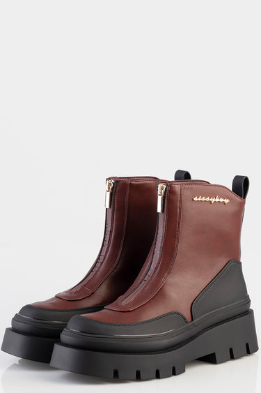 brown leather ankle boots with black chunky lug sole, side gold zippers, and back pull tabs