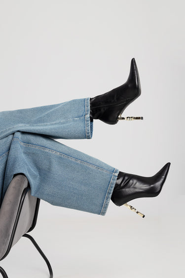 feet in black pointed toe boots with a metallic heel, paired with light blue denim jeans