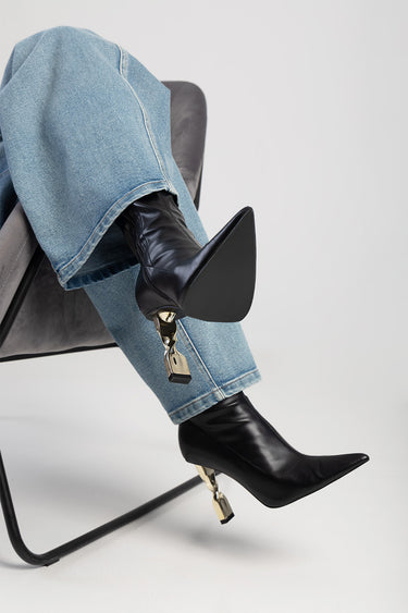 black leather pointed toe boot with a gold metal accessory at the heel paired with blue jeans