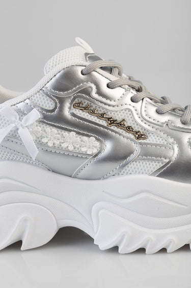 blue jean traders silver and white chunky sneaker with mesh panels, lace details, a white ribbon bow, and gold script logo