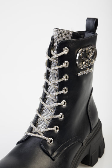 black ankle boot with rhinestone tongue, silver laces through metal eyelets, and a chunky sole with a metal emblem on the