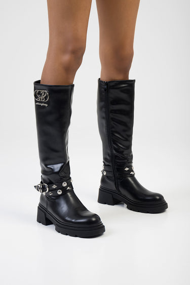 black knee high boots by Blue Jean Traders with a silver logo on the shaft and studded ankle straps on a chunky sole