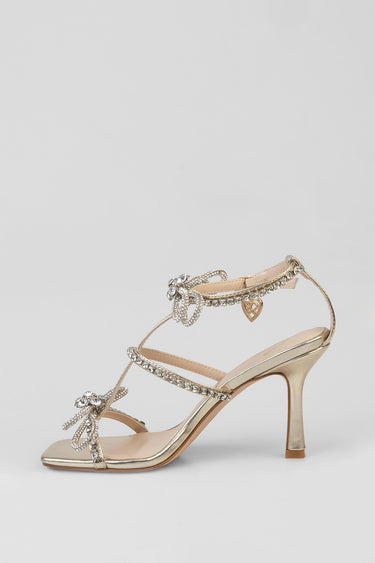 gold tone stiletto sandal with crystal embellishments, open toe, ankle strap with heart pendant and bow decorations