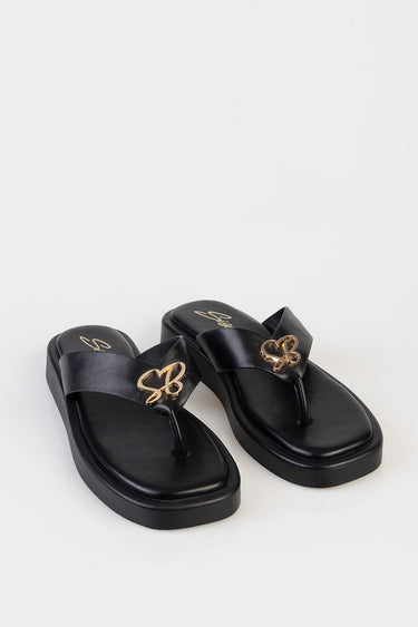 black slide sandals with a wide strap and gold emblem on the strap