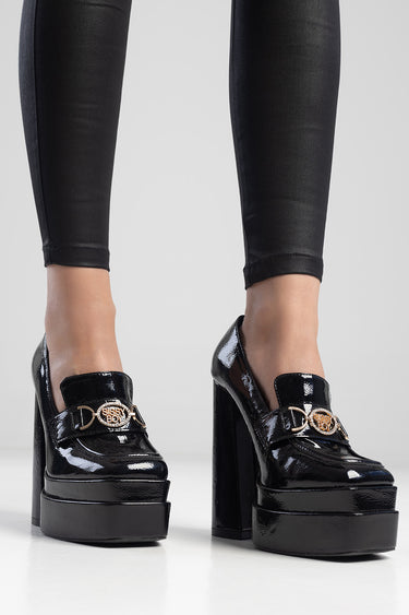 woman wearing black patent platform heels with gold horsebit detail and chunky heel