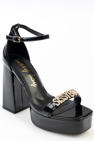 black patent platform block heel sandal with ankle strap and gold logo embellishment across the toe